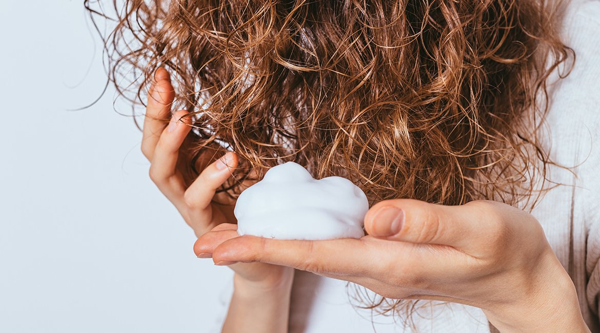 Haarschaum wird auf welliges braunes Haar aufgetragen